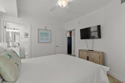 a white bedroom with a large bed and a flat screen tv at Palazzo Unit 301 by 30A Escapes in Panama City Beach