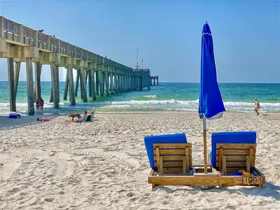 two chairs and an umbrella on a beach with a pier at Palazzo Unit 301 by 30A Escapes in Panama City Beach