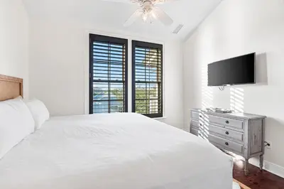 a white bedroom with a bed and a flat screen tv at Rosemary Thyme by 30A Escapes in Rosemary Beach