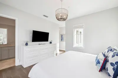 a white bedroom with a television on a white dresser at Three Amigos Gulf Front by 30A Escapes in Seagrove Beach