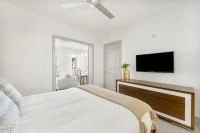a white bedroom with a bed and a flat screen tv at The Pointe Unit 122 by 30A Escapes in Rosemary Beach