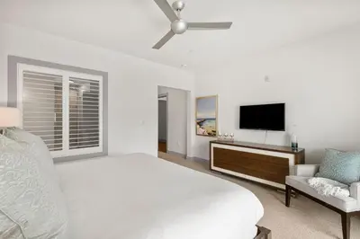 a white bedroom with a bed and a flat screen tv at The Pointe Unit 122 by 30A Escapes in Rosemary Beach