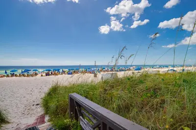 a sandy beach with people sitting under umbrellas at Shores of Panama by Blue Swell in Panama City Beach