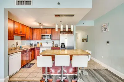 a kitchen with wooden cabinets and a island with bar stools at Panama City Beach Condo - Walk to the Ocean! in Panama City Beach