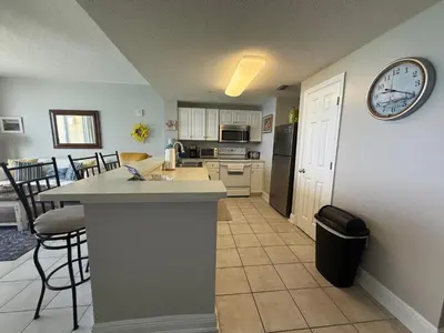 a kitchen and living room with a counter and a clock on the wall at Majestic Beach Towers 905 in Panama City Beach