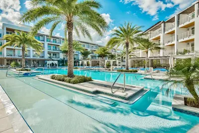 a swimming pool with palm trees in front of a building at The Pointe Unit 326 by 30A Escapes in Rosemary Beach