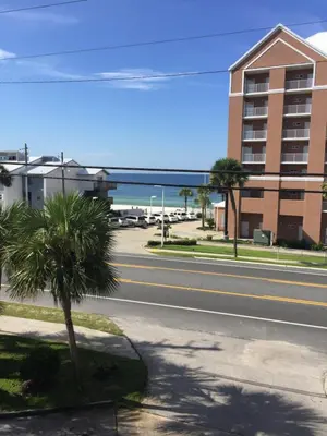 a street with a palm tree and a building and the ocean at Beach Place Seconds to Beach 23 in Panama City Beach