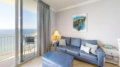 a living room with a blue couch and a balcony at Tidewater 2714 in Panama City Beach