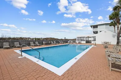 a swimming pool with chairs and a building at Howdy Beach by 30A Escapes in Panama City Beach