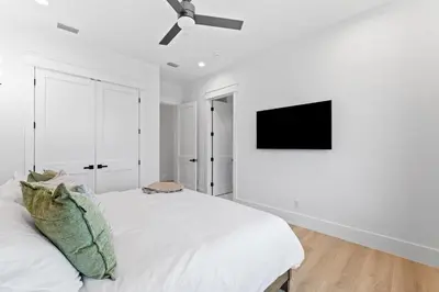 a white bedroom with a bed and a flat screen tv at Jewel of Oleander by 30A Escapes in Panama City Beach