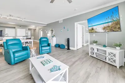a living room with blue chairs and a large screen at Tidewater 2308 by Emerald Coast Retreats in Panama City Beach