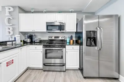 a kitchen with white cabinets and a stainless steel refrigerator at Tidewater 2308 by Emerald Coast Retreats in Panama City Beach