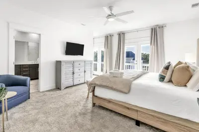a white bedroom with a large bed and a blue chair at Salty Sons 4 BR and just minutes to the Beach Rosemary and 30Avenue in Inlet Beach