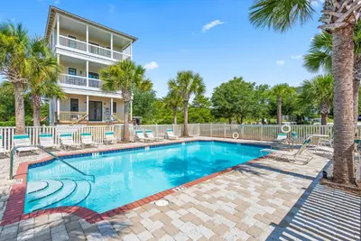 a swimming pool with palm trees and a house at Salt & Light - 5 BR, Sleeps 18, Gulf & Lake Views, Game Room & Bikes in Seagrove Beach