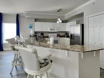 a kitchen with white cabinets and a counter with chairs at Tidewater Beach Resort #1501 in Panama City Beach
