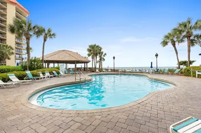 a swimming pool with chairs and palm trees and the ocean at Summerhouse Beach Resort by Panhandle Getaways in Panama City Beach