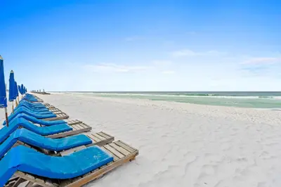 a row of blue lounge chairs on a beach at Summerhouse Beach Resort by Panhandle Getaways in Panama City Beach