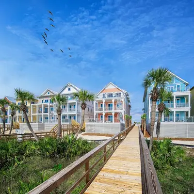 a boardwalk leading to a beach with palm trees and buildings at Margaritaville Beach Cottage Resort Panama City Beach in Panama City Beach