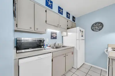 a kitchen with white cabinets and a sink and a refrigerator at Nautical Watch E-3 in Panama City Beach