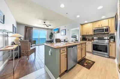 a kitchen with wooden cabinets and a dining room with a table at Sterling Reef 1504 in Panama City Beach