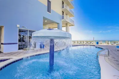 a swimming pool with a fountain in front of a building at Walk to Shore Panama City Beach Condo with Pool in Panama City Beach