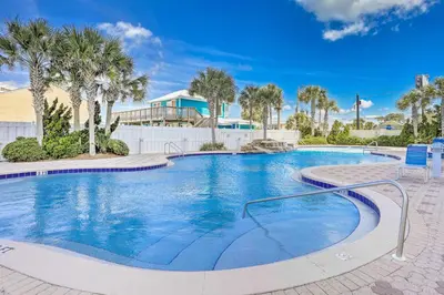 a large swimming pool with palm trees and a building at Walk to Shore Panama City Beach Condo with Pool in Panama City Beach