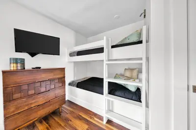 a bedroom with white bunk beds and a flat screen tv at Gulf Views! Only 30 Seconds to the beach Modern Amenities Meets Vintage Charm in Inlet Beach