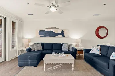 a living room with a blue couch and a table at Newly Renovated Village Condo! Easy Beach & Pool Access! in Rosemary Beach