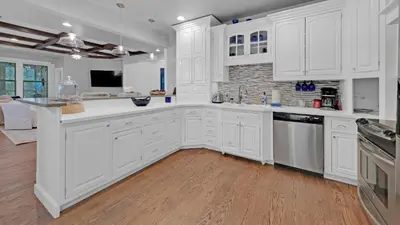 a white kitchen with white cabinets and wooden floors at Luxury Seacrest Beach Home Community Pool Deeded Beach Access! in Rosemary Beach