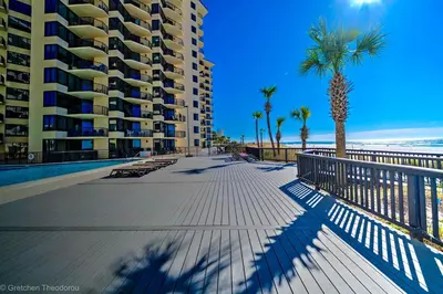 a boardwalk next to a beach with a building and palm trees at Sunbird Resort! Ground-Floor Renovated Beach Condo! Free Beach Chairs! by Dolce Vita Getaways PCB in Panama City Beach