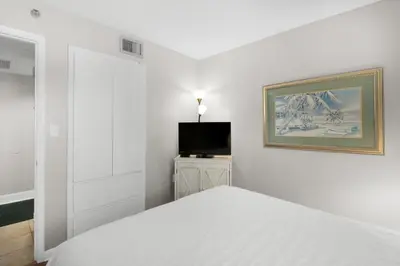 a white bedroom with a bed and a television at Sunbird 601W in Panama City Beach