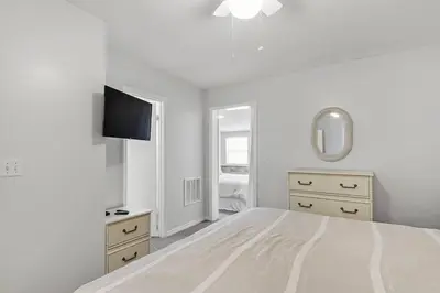 a white bedroom with a bed and a tv at The Original Robin's Nest/ 5 Min Walk To The Beach in Panama City Beach