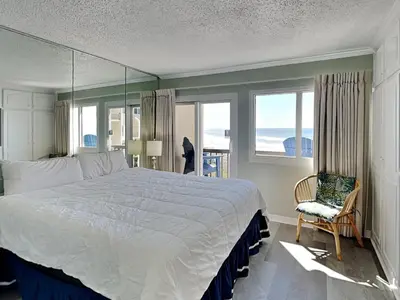 a bedroom with a bed and a chair and windows at Pinnacle Port a-702 in Panama City Beach