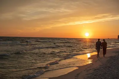 two people walking on the beach at sunset at Gulf-Front Shores of Panama Condo w/ Balcony & Resort Amenities in Panama City Beach