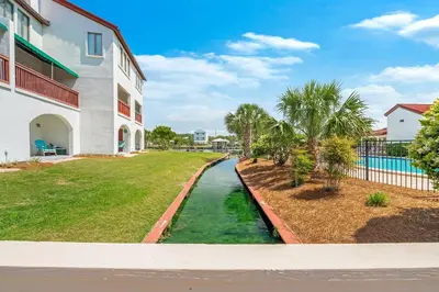 a canal in front of a building with palm trees at The Beachy Boater at St Thomas Square #305 by Nautical Properties in Panama City Beach