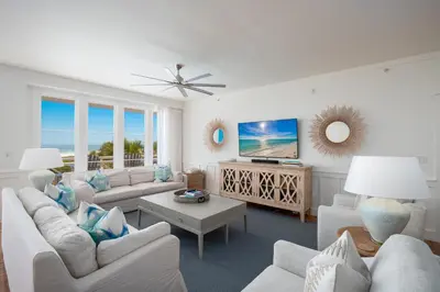 a living room with white furniture and a tv at Gulf Front - Large Pool - Bikes - Gated Community in Inlet Beach