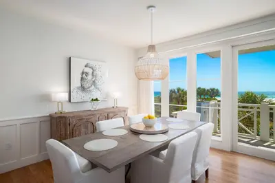 a dining room with a wooden table and white chairs at Gulf Front - Large Pool - Bikes - Gated Community in Inlet Beach