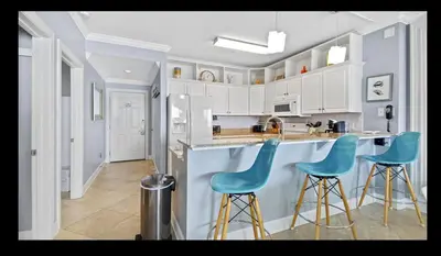 a kitchen with blue bar stools and white cabinets at Beautiful Beachfront Views - The Retreat at Emerald Isle in Panama City Beach