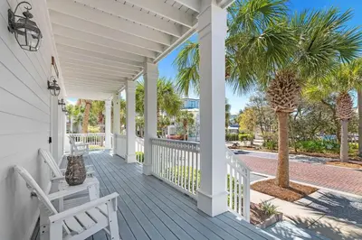 a white porch with two white chairs and palm trees at Sugar Beach Cottage in Inlet Beach