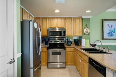 a kitchen with wooden cabinets and stainless steel appliances at Beachfront Bliss Luxe 3BR Condo at Marisol Complex in Panama City Beach