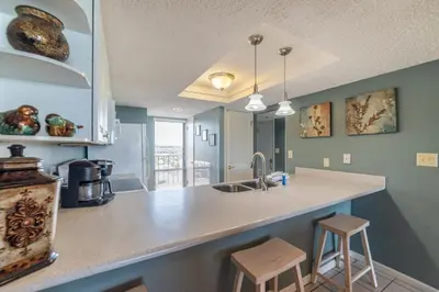 a kitchen with a sink and a counter with stools at Edgewater 3-0404 'Isle Be Back' in Panama City Beach