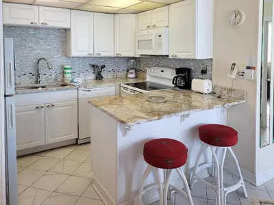a kitchen with white cabinets and red bar stools at Sunbird 0405E 'No Worries' in Panama City Beach