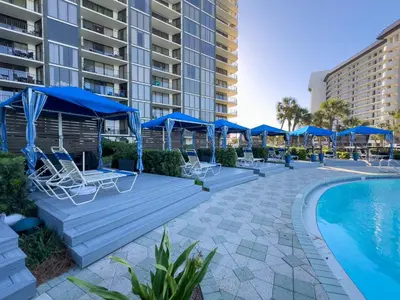 a swimming pool with blue umbrellas and chairs next to a resort at Edgewater 1-0303 'Salty Sunsets' in Panama City Beach