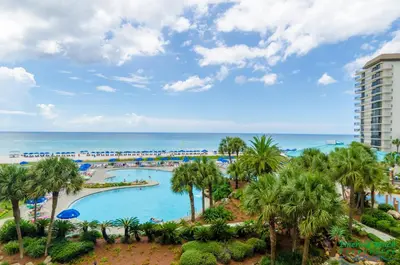 an aerial view of a resort pool with palm trees and the ocean at Edgewater 3-1010 'The Salty Coconut' in Panama City Beach