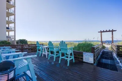 a deck with blue chairs and a grill and the beach at Top Of The Gulf 312 'The Tip-Sea Turtle' in Panama City Beach