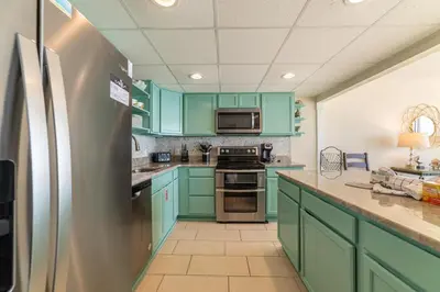 a kitchen with green cabinets and a stainless steel refrigerator at Edgewater 1-1212 'Combee's Penthouse HideAway' in Panama City Beach
