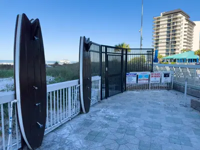 a black gate with a surfboard next to a beach at Edgewater 3-0814 'Pelican Watch' in Panama City Beach