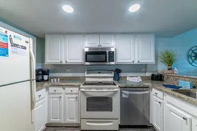 a kitchen with white cabinets and a stove and a microwave at Mariner West 605 'Flip Flops & Sunsets' in Panama City Beach