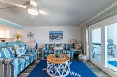 a living room with blue couches and a table at Mariner West 605 'Flip Flops & Sunsets' in Panama City Beach