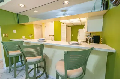 a kitchen with three green bar stools and a mirror at Edgewater Villa 3005 'Paradise Palms' in Panama City Beach